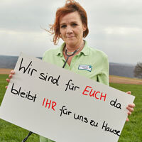 Eine Pflegerin des Haus Kleineichen mit dem Schild "Wir sind für euch da – bleibt ihr für uns zu Hause."